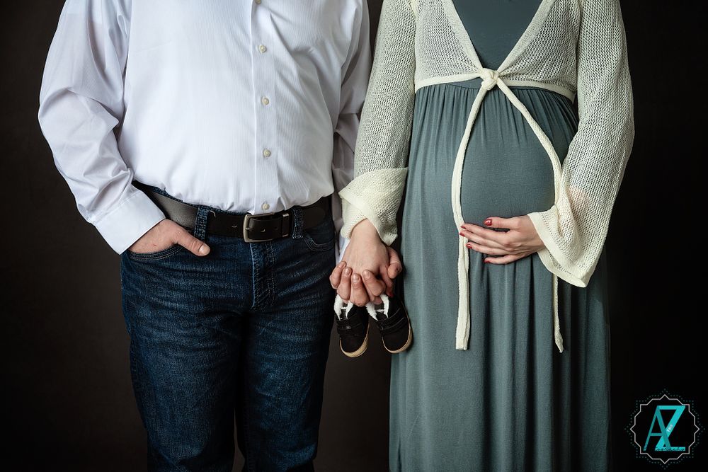 Close-up of couple holding baby shoes during maternity photoshoot.