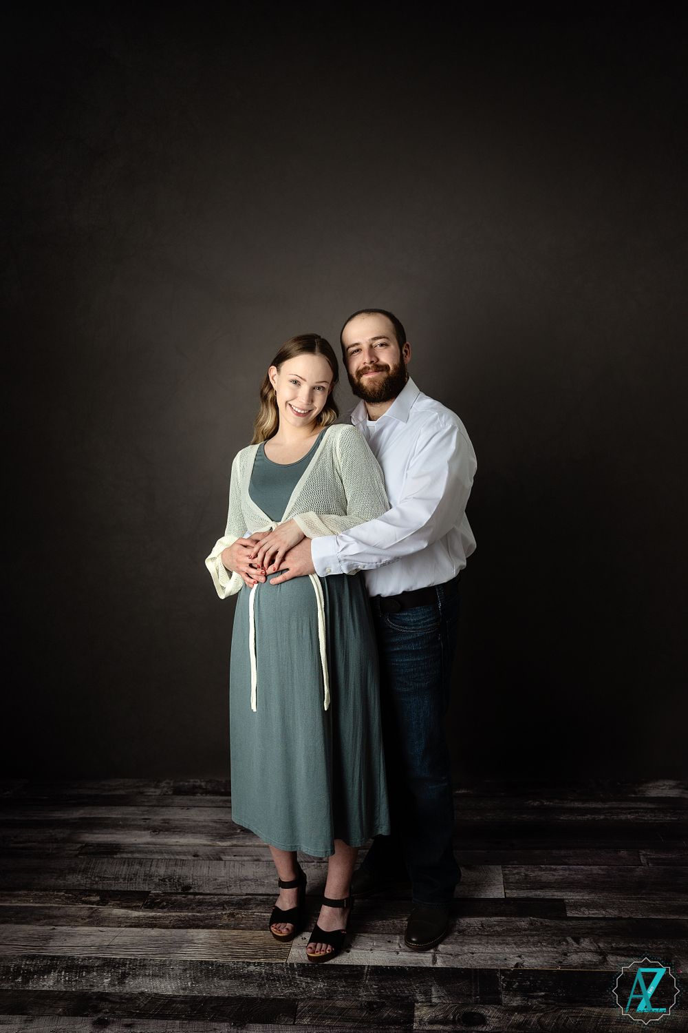 Elegant maternity portrait with couple embracing against dark studio background.
