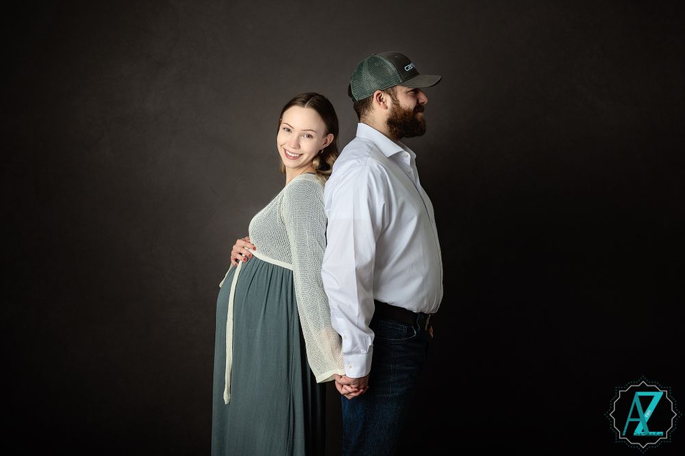Back-to-back maternity pose against dark backdrop in studio setting.