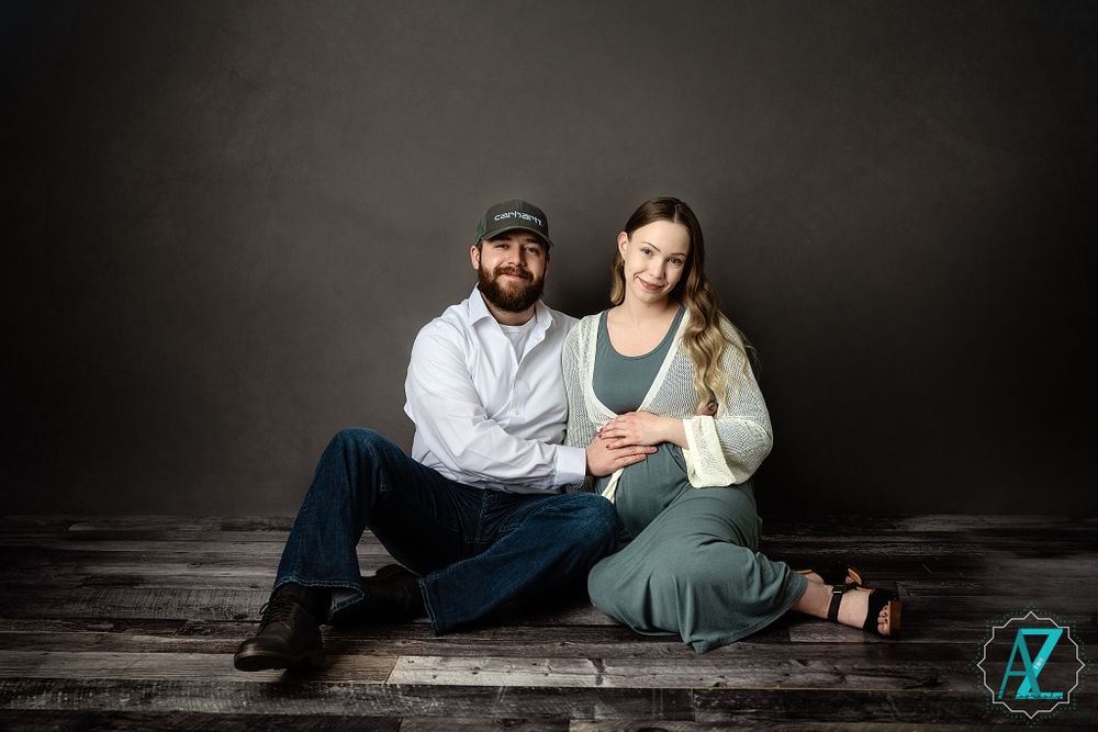 An intimate studio portrait session featuring a couple seated on rustic wooden flooring.