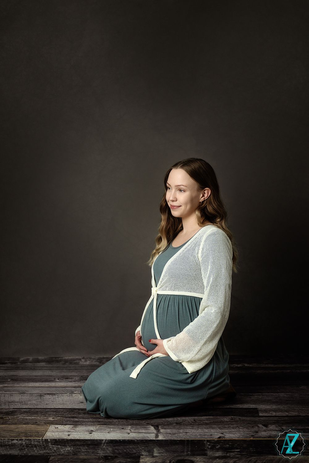 Serene maternity portrait featuring a woman in sage dress against dark backdrop.