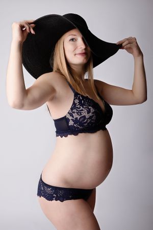 Maternity boudoir photo featuring black sun hat and navy lace lingerie.