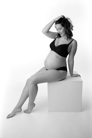 Black and white maternity portrait of seated figure in intimate wear.