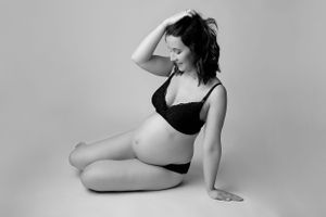 Studio maternity portrait in black and white with minimalist styling.