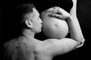 Artistic black and white maternity photo showing a tattooed person tenderly touching a pregnant belly.