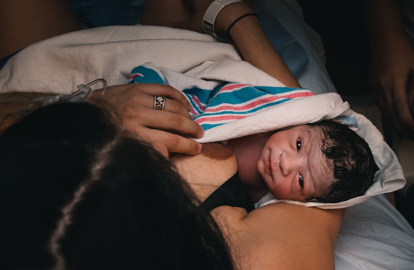 woman cradles baby while baby looks up after natural hospital birth