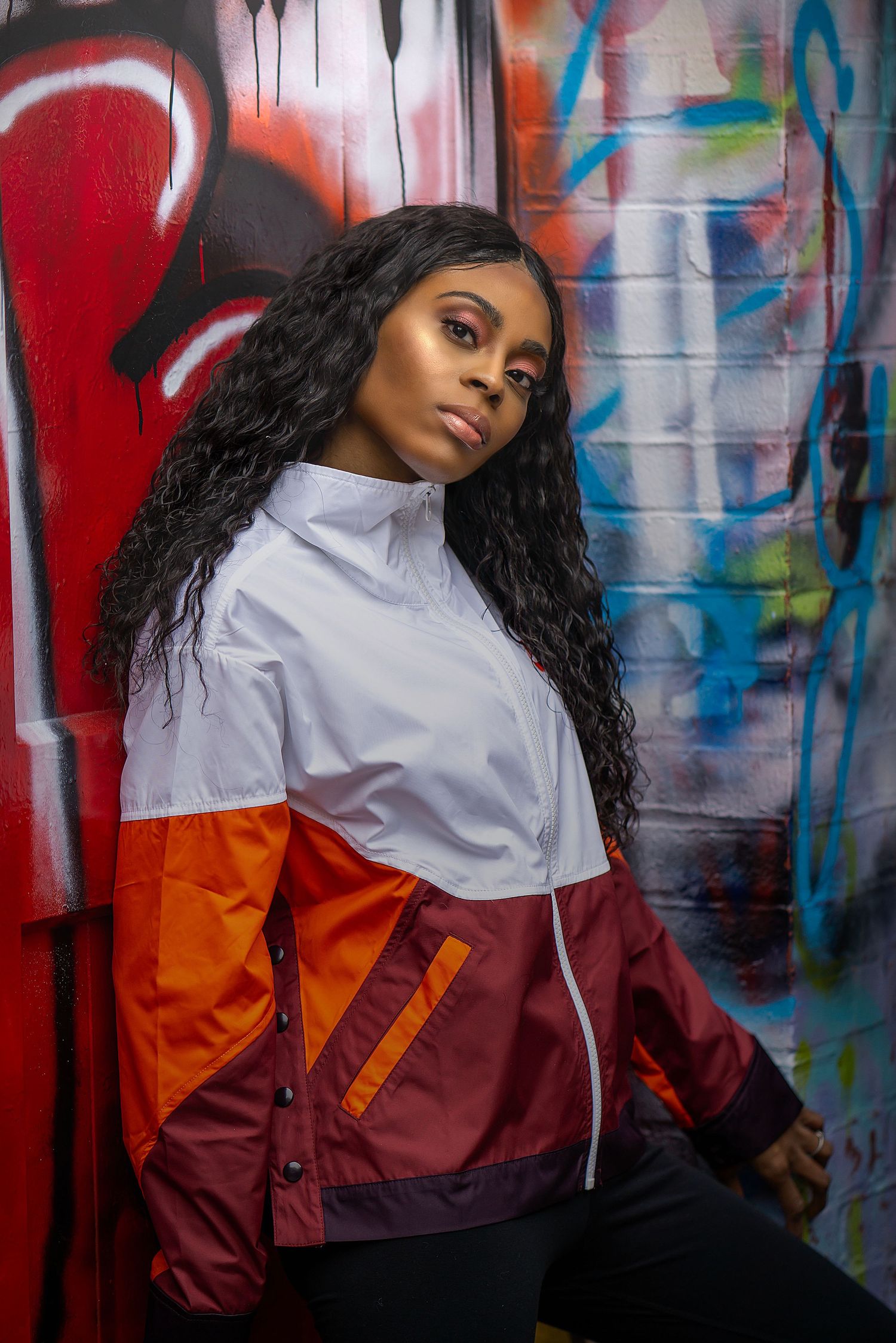 Street fashion portrait against graffiti backdrop wearing color block windbreaker jacket.