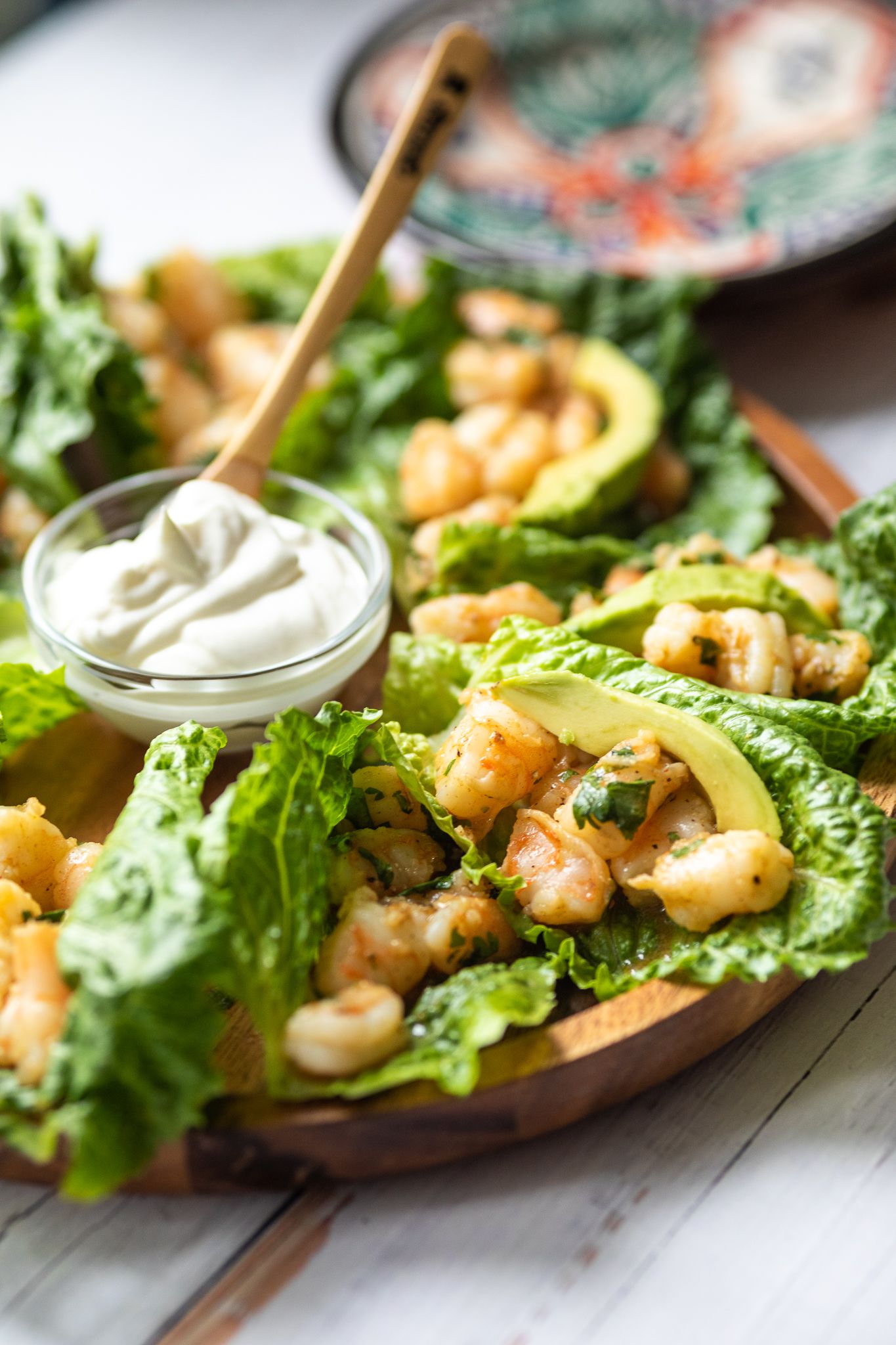 Fresh shrimp lettuce wraps garnished with avocado and white sauce on a wooden serving board.