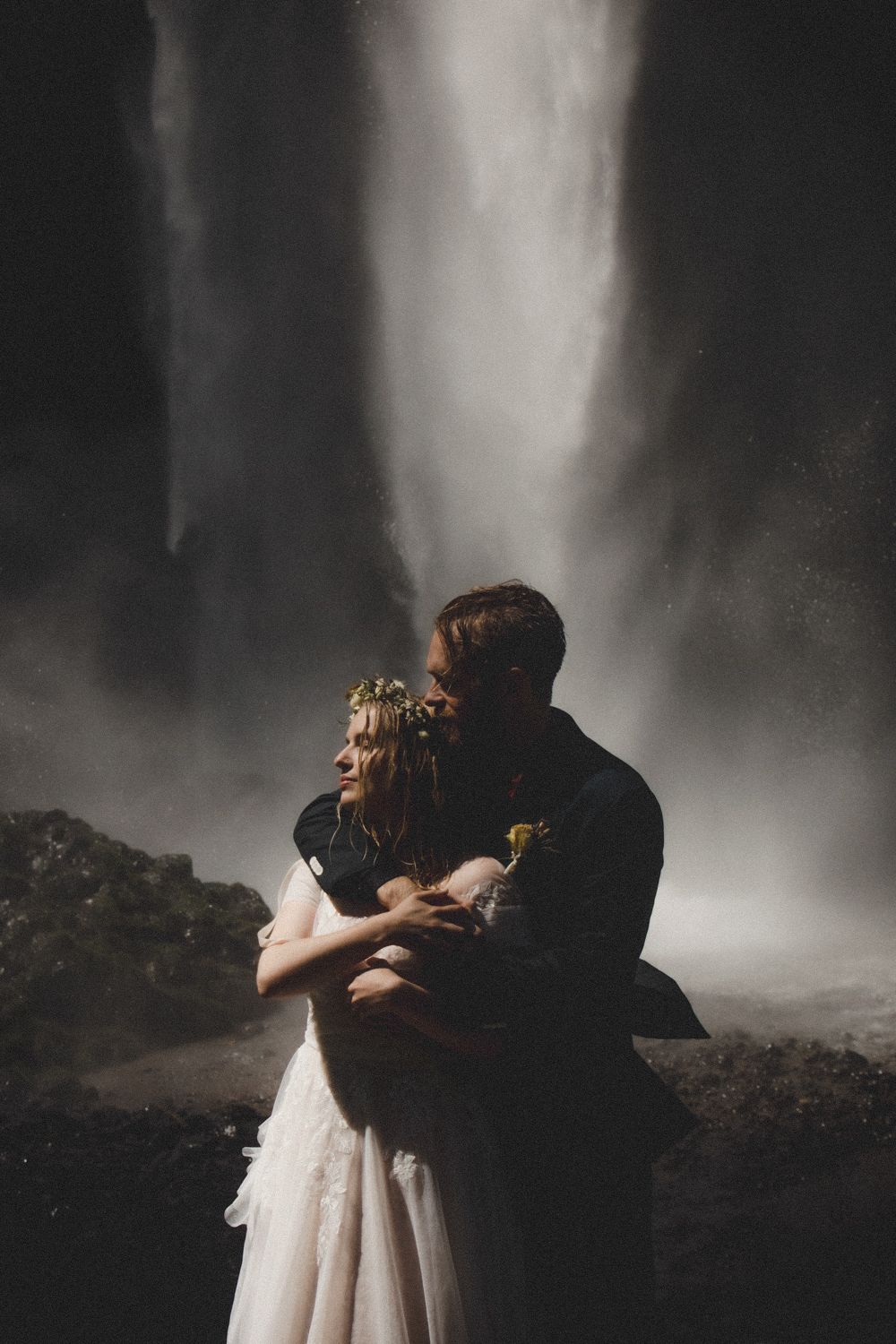 Romantic embrace between newlyweds with a misty waterfall creating a dramatic backdrop.