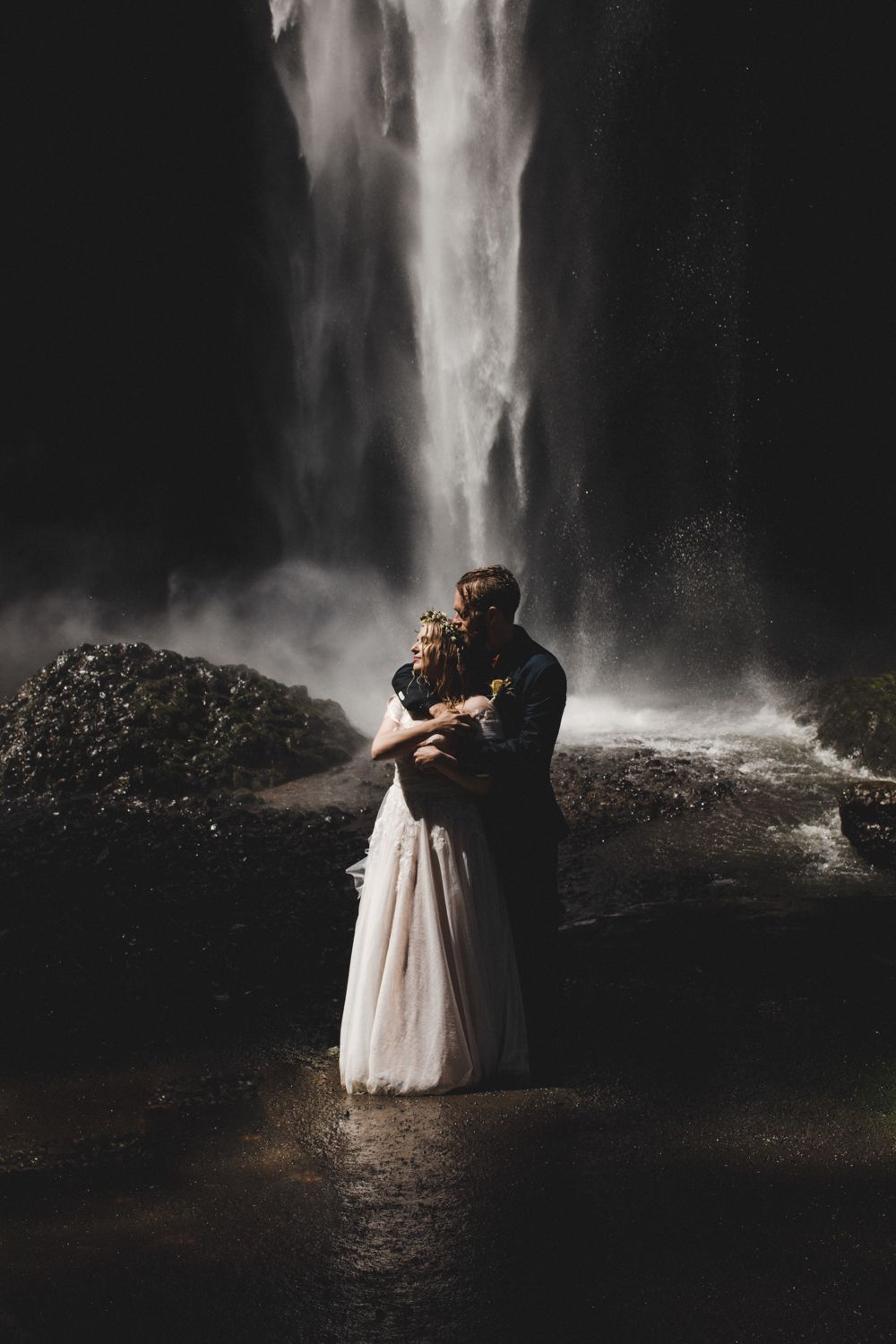 Intimate moment between newlyweds embracing in front of a powerful waterfall.