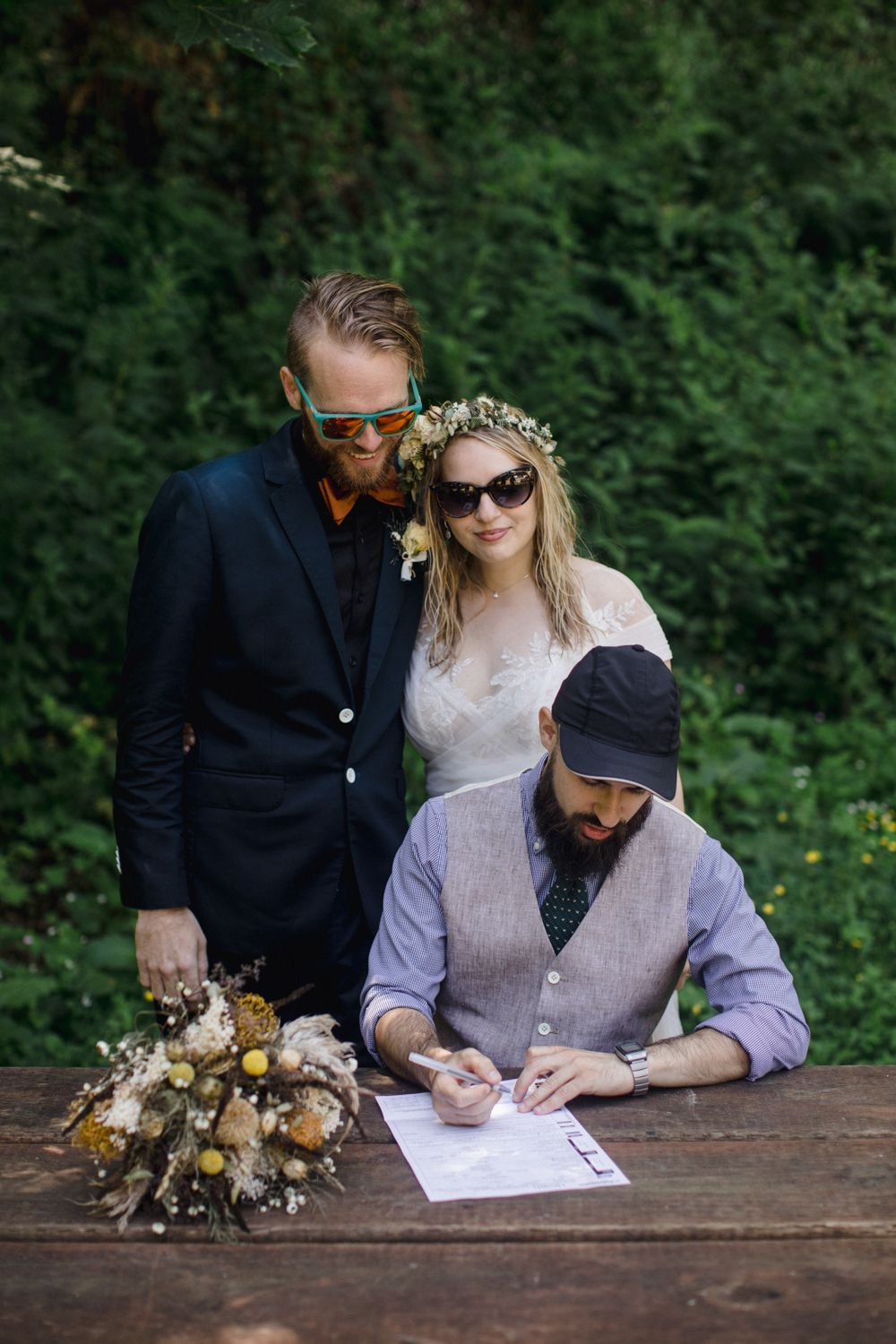Wedding ceremony document signing at wooden table in lush forest setting.