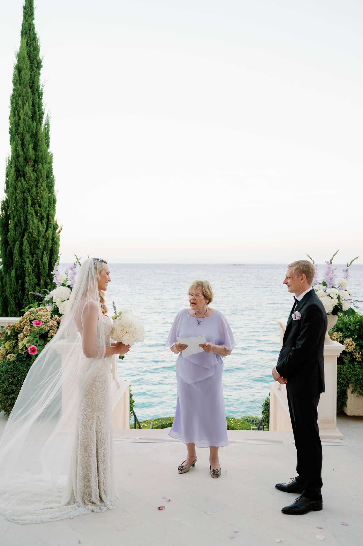 Wedding ceremony setup with ocean backdrop and tall cypress trees.