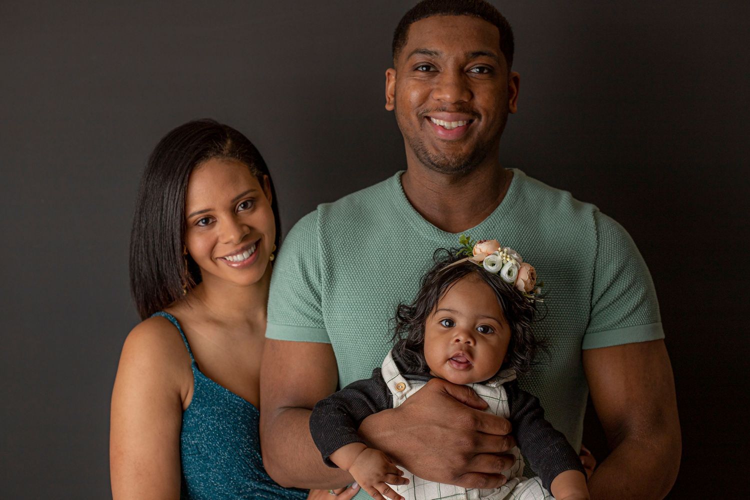 Studio portrait of family in coordinated outfits against dark background.