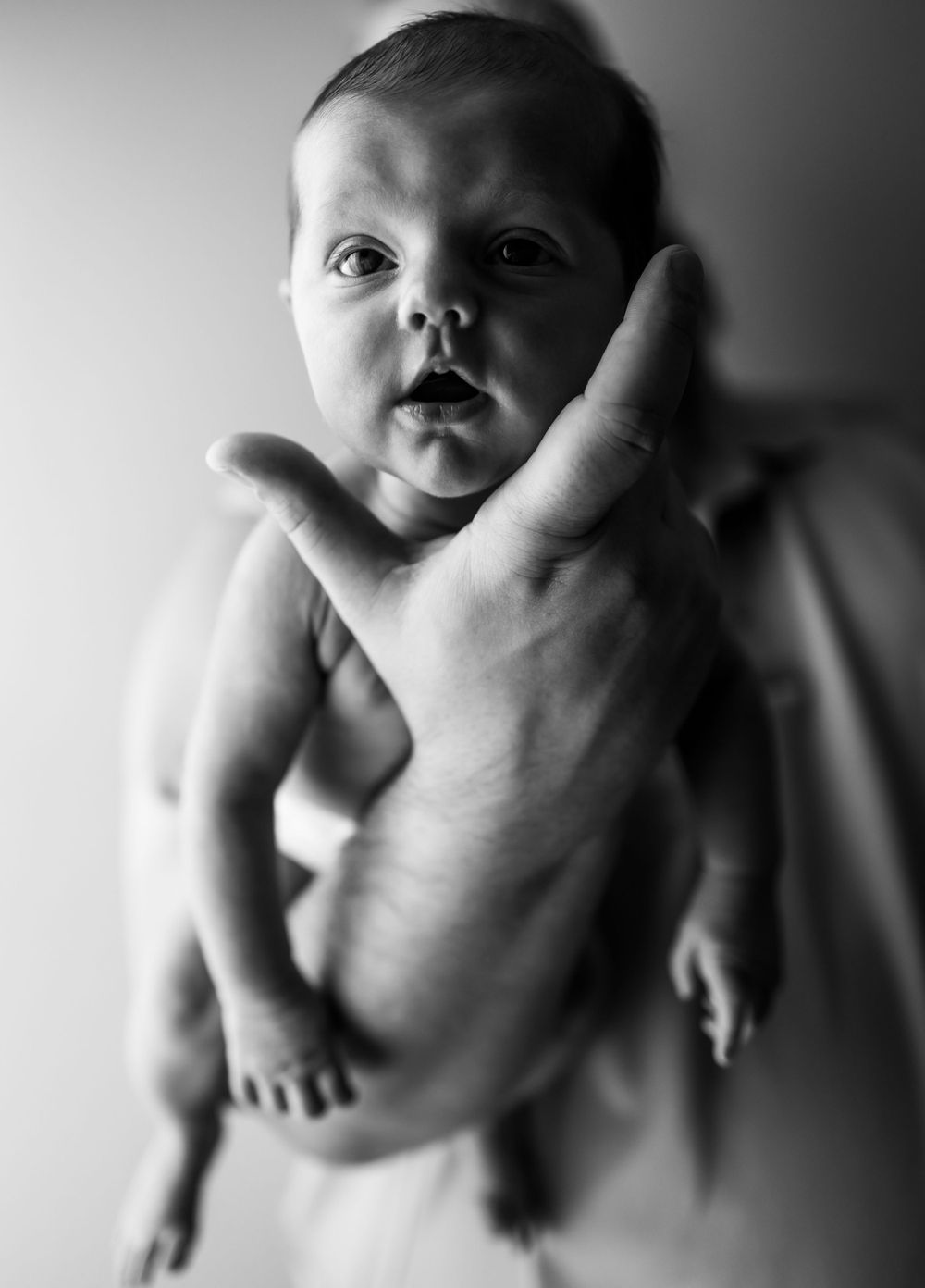 A black and white portrait of an infant being held by an adult hand.