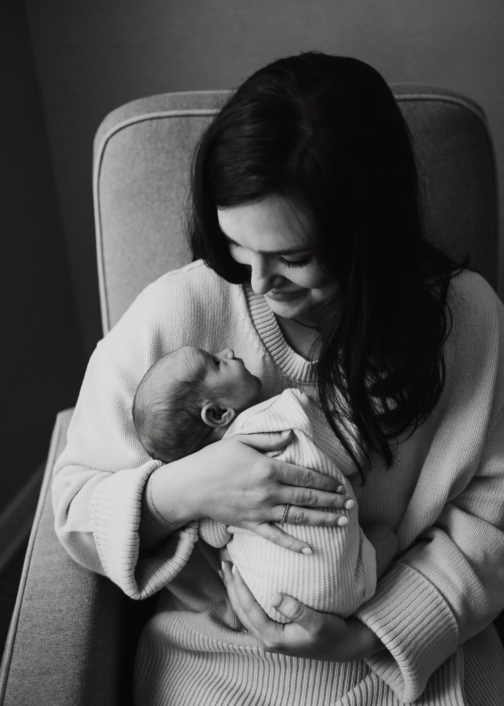 Black and white photo showing tender moment between parent and infant in cozy chair.