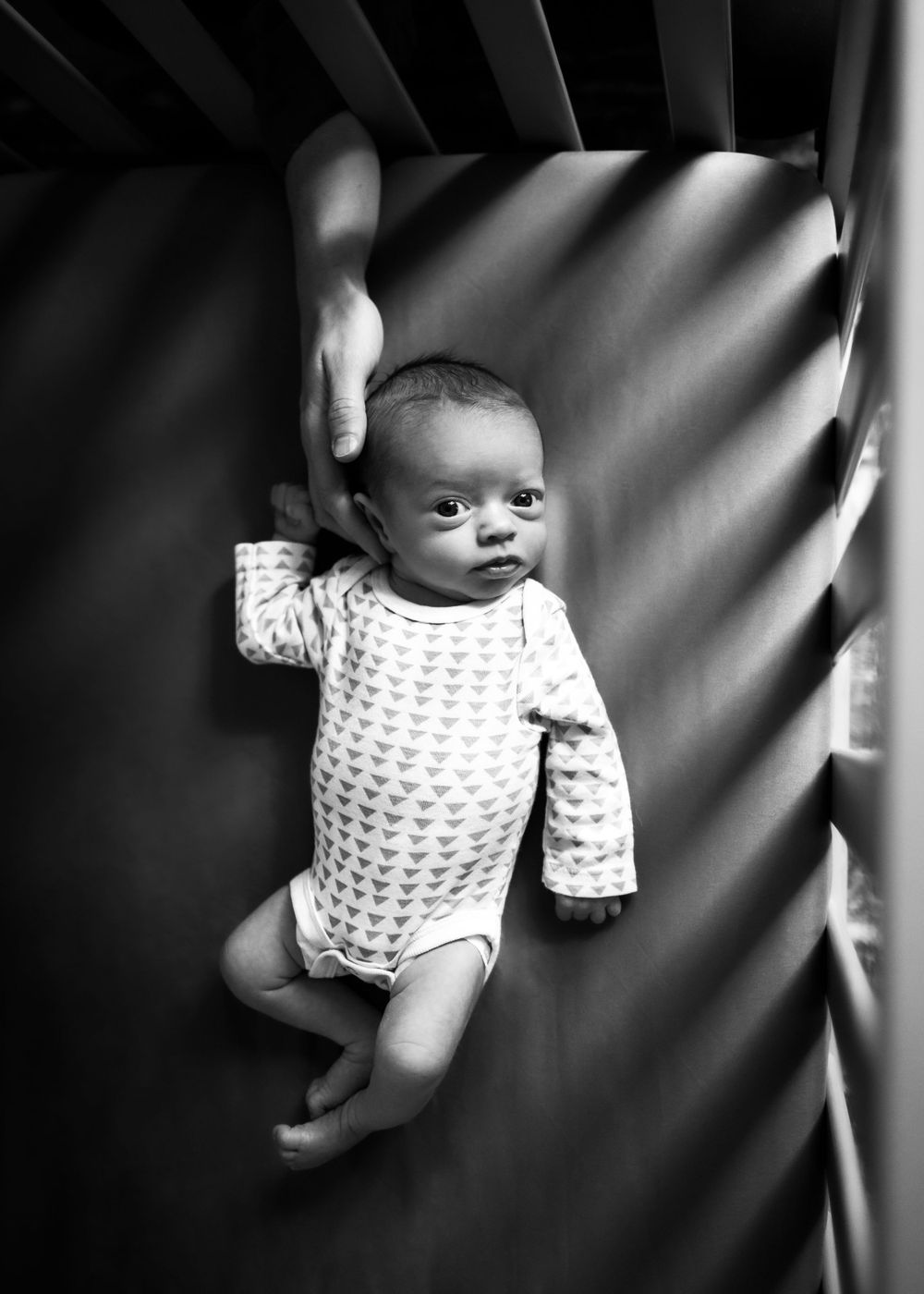 Black and white portrait of baby in patterned onesie against dramatic window light.