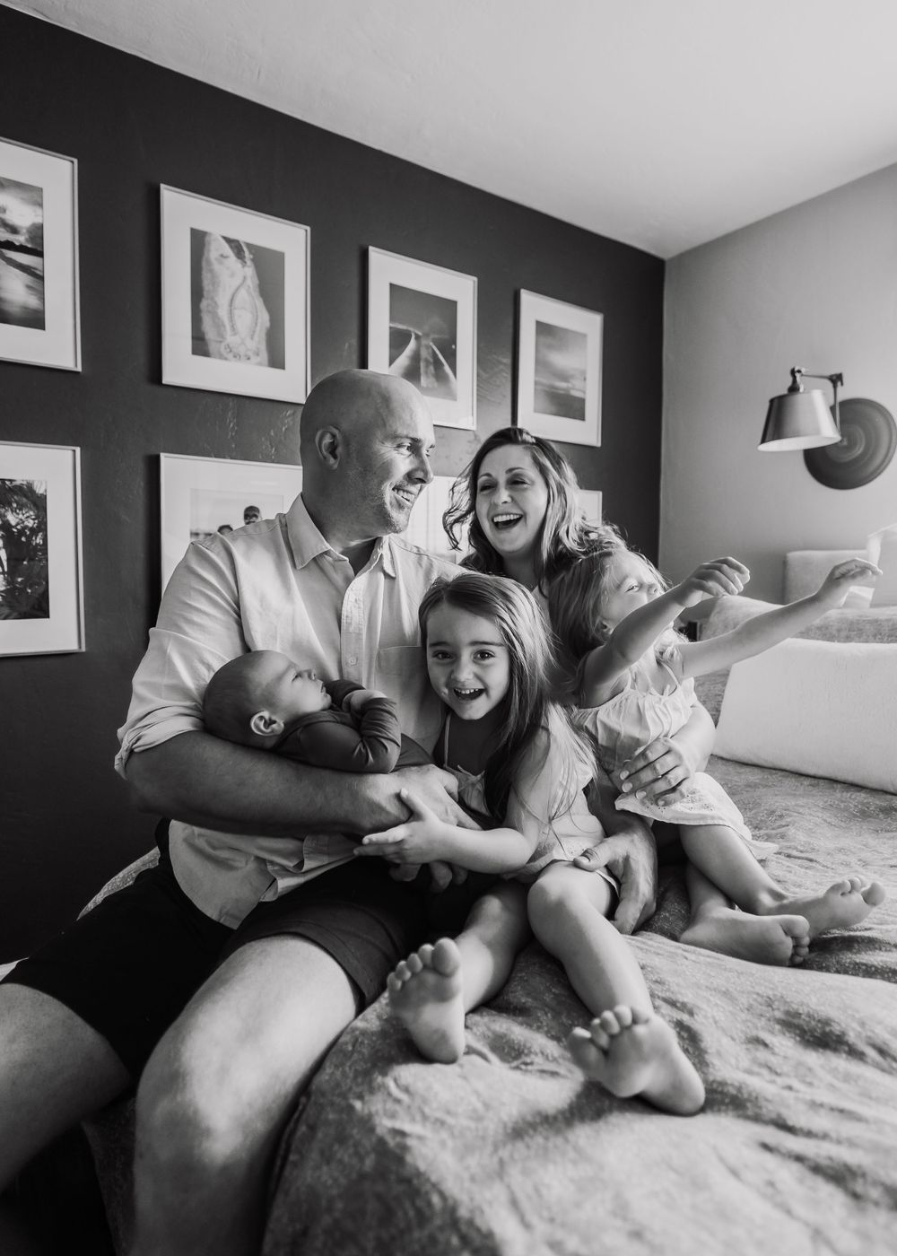 Black and white candid family moment on bed with gallery wall backdrop.