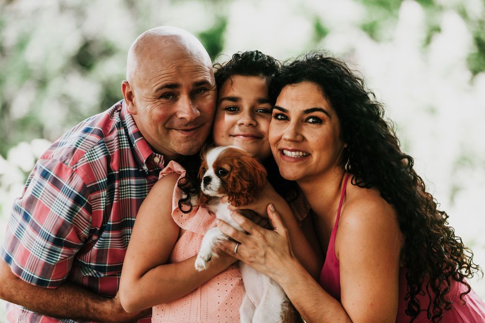 A happy family poses together with their small brown dog for a cheerful portrait.