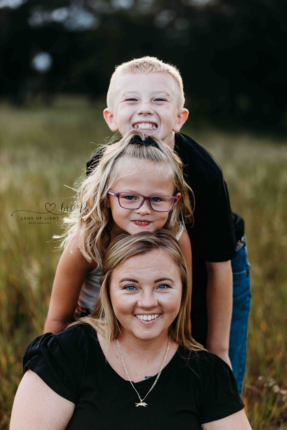 Family portrait with bright smiles stacked vertically in outdoor field setting.