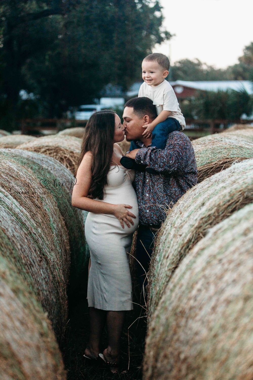 A romantic moment between a couple by hay bales in a rustic outdoor setting.