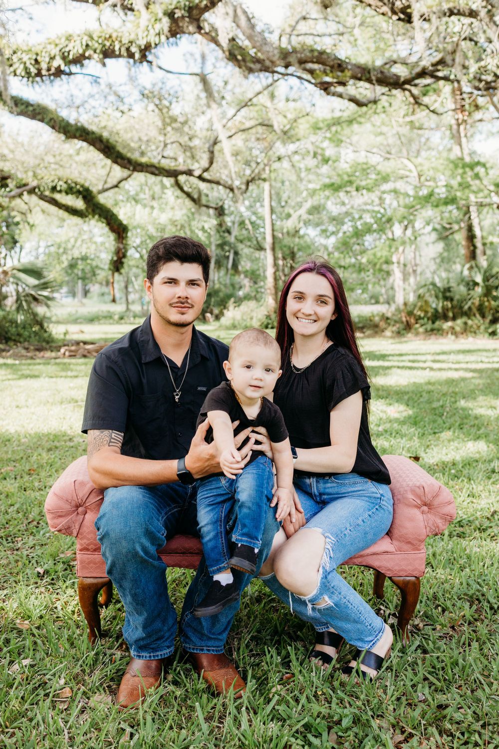 A family portrait on a pink velvet couch in a sunny outdoor garden setting.