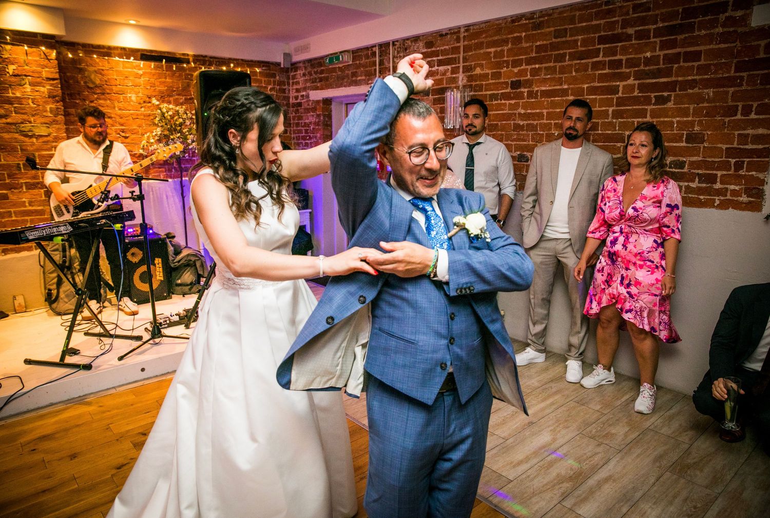 Wedding couple dances in a rustic brick venue with guests watching from the sides.