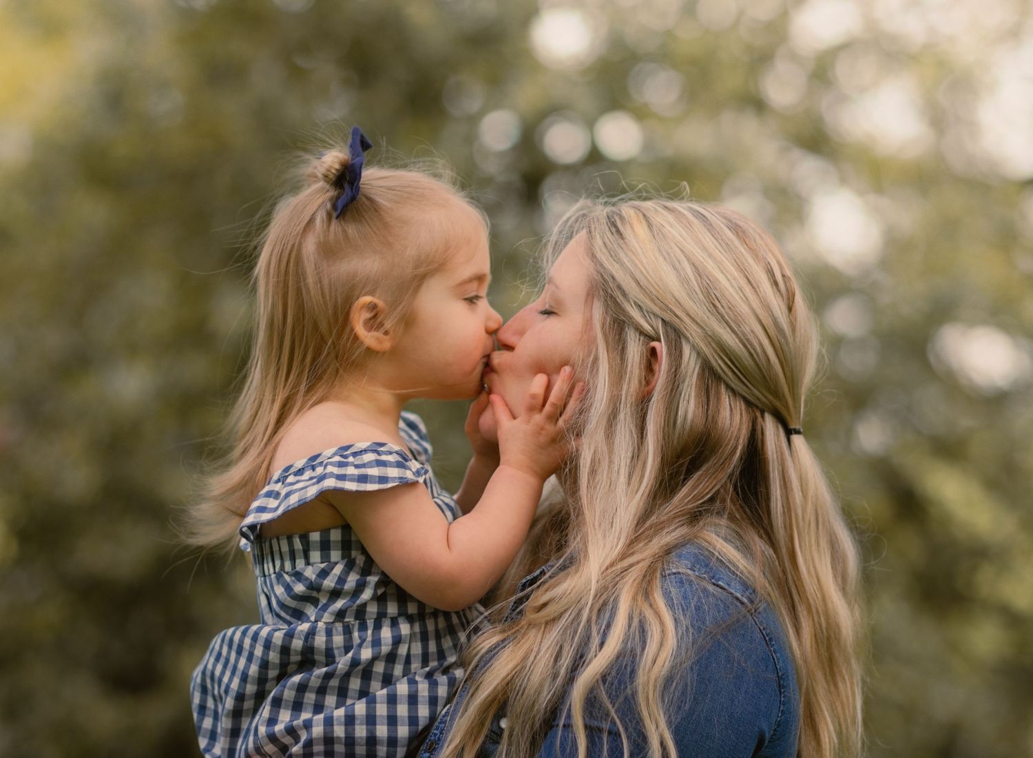 mama holding big sister and kissing. blonde hair and blue eyes. very cute.