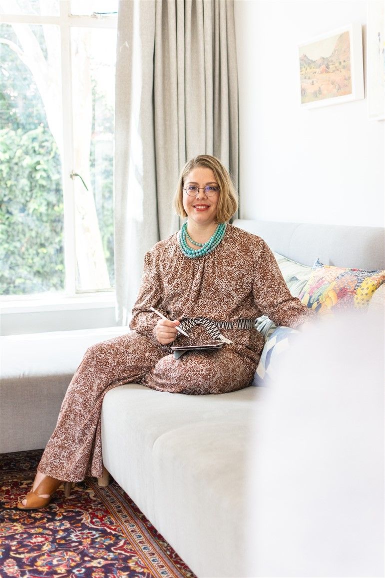 Person relaxing on white couch wearing floral print outfit and turquoise necklace.