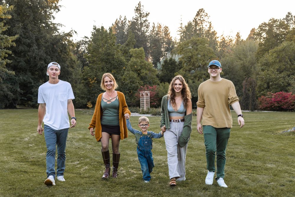 Family walking together on grass with trees in background during fall season.