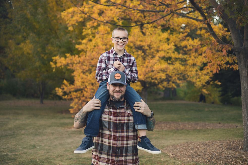 Father gives child piggyback ride in autumn park with golden leaves.
