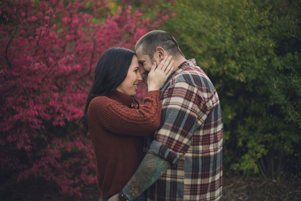 A couple shares an intimate moment against a backdrop of pink and green autumn foliage.