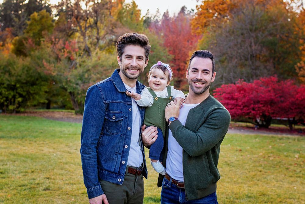 Three people pose together outdoors with colorful fall foliage in the background.