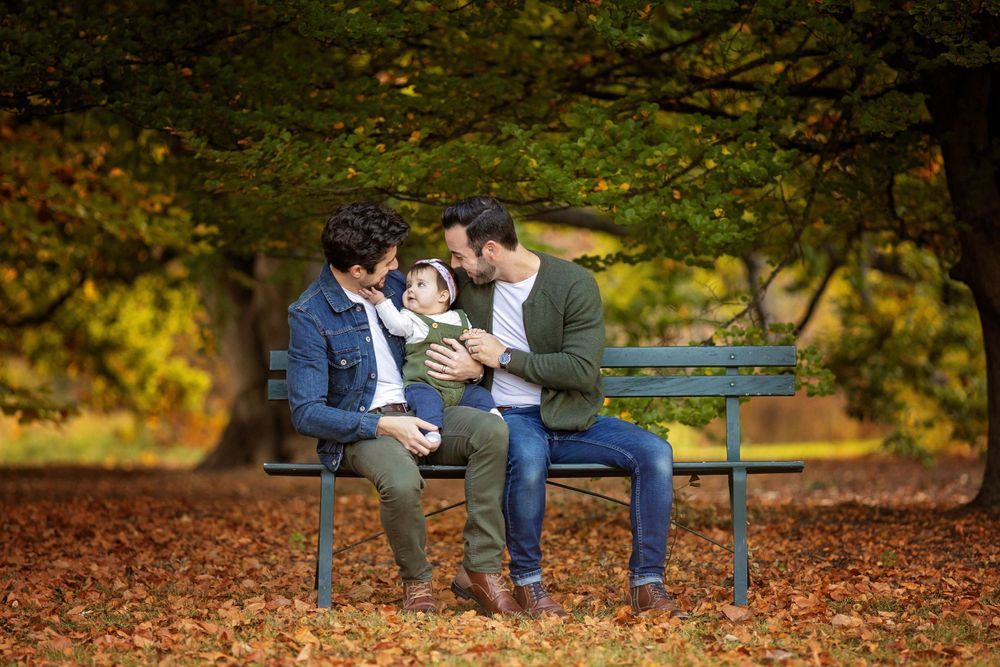 Three people sit close together on a blue bench surrounded by fallen autumn leaves.