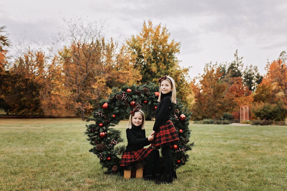 Holiday portrait with decorated wreath against autumn foliage backdrop.