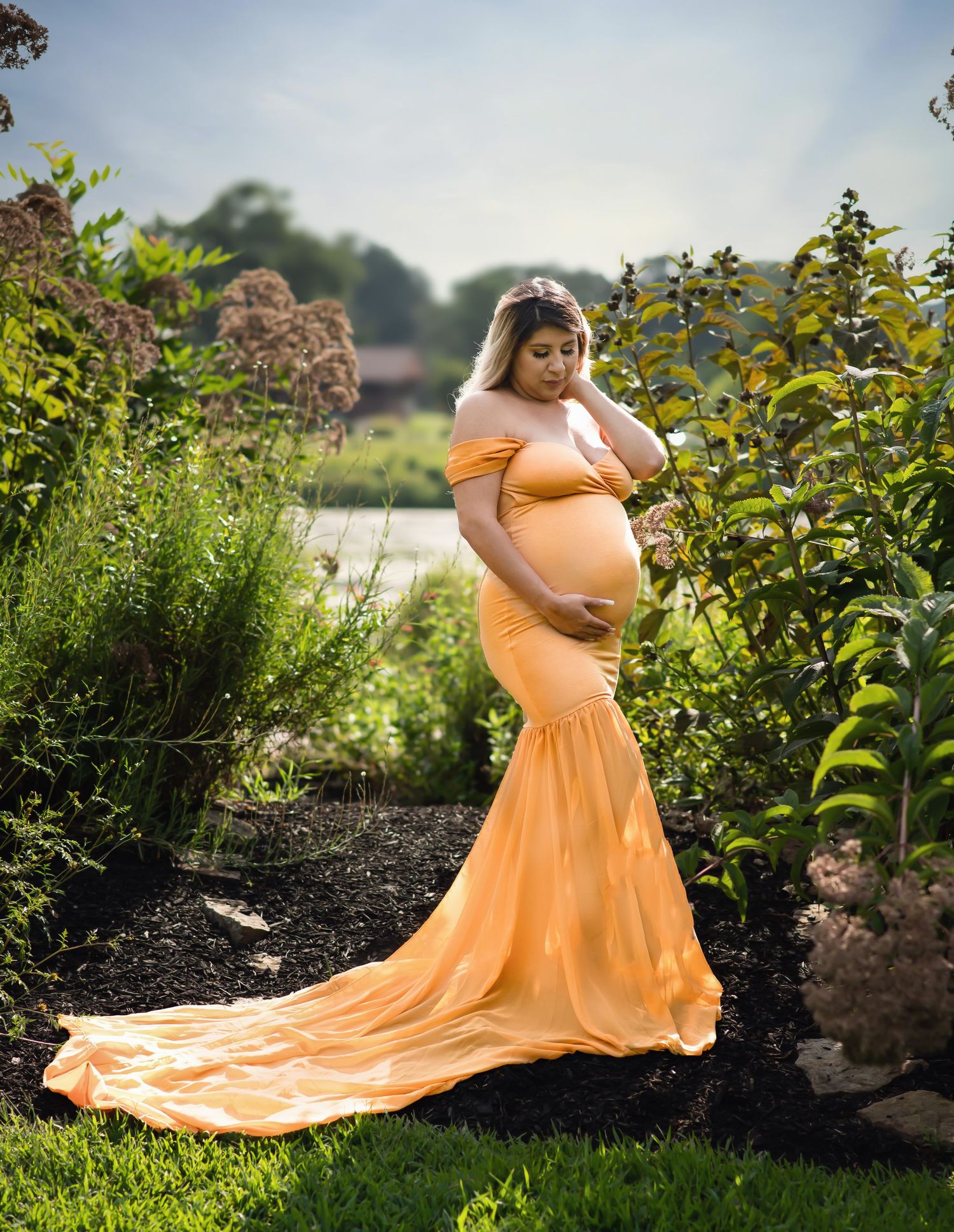 Maternity photo featuring flowing peach gown in garden setting with trailing train.
