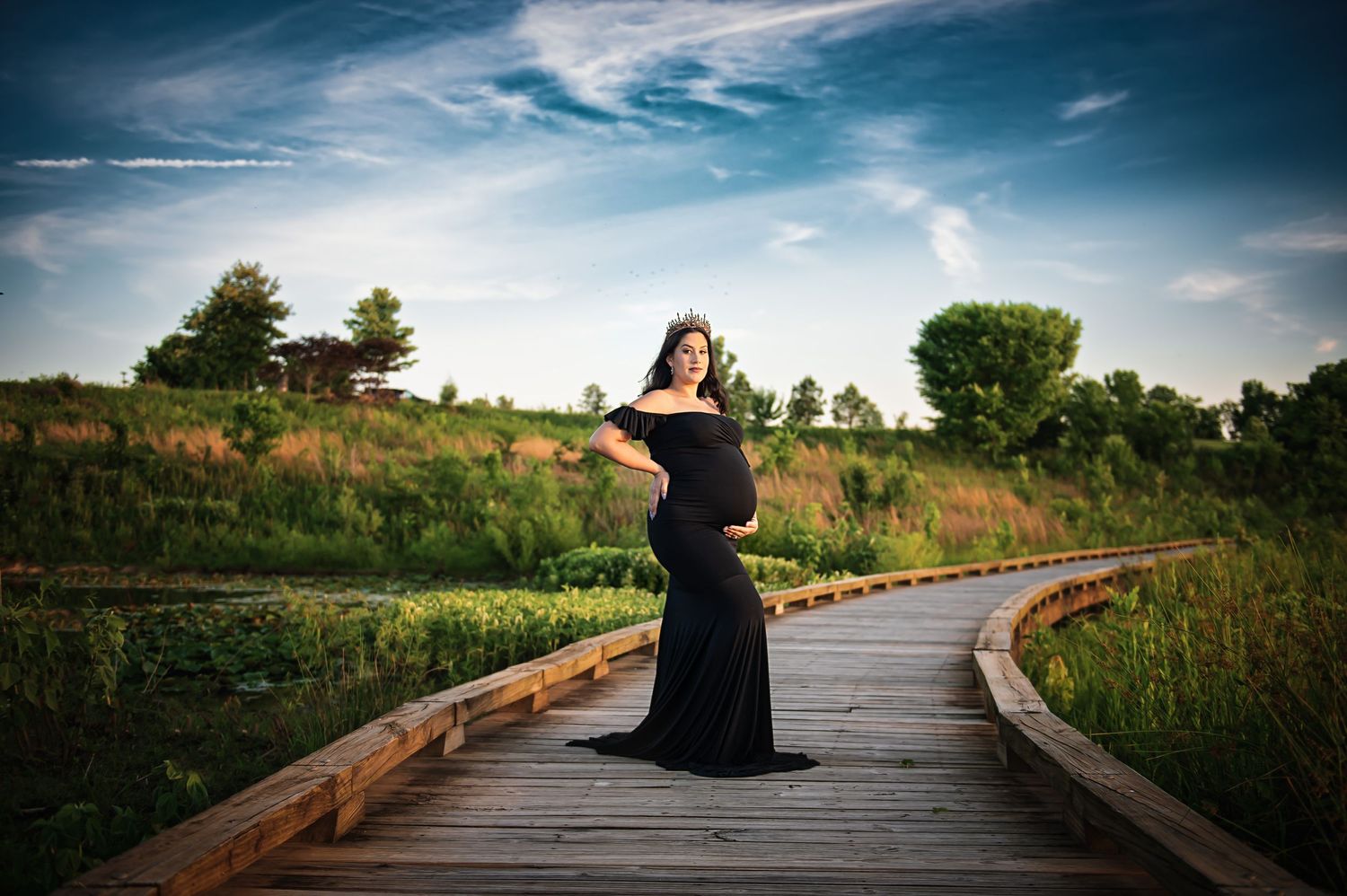 Silhouette maternity photo on wooden boardwalk against dramatic sky and tall grass.