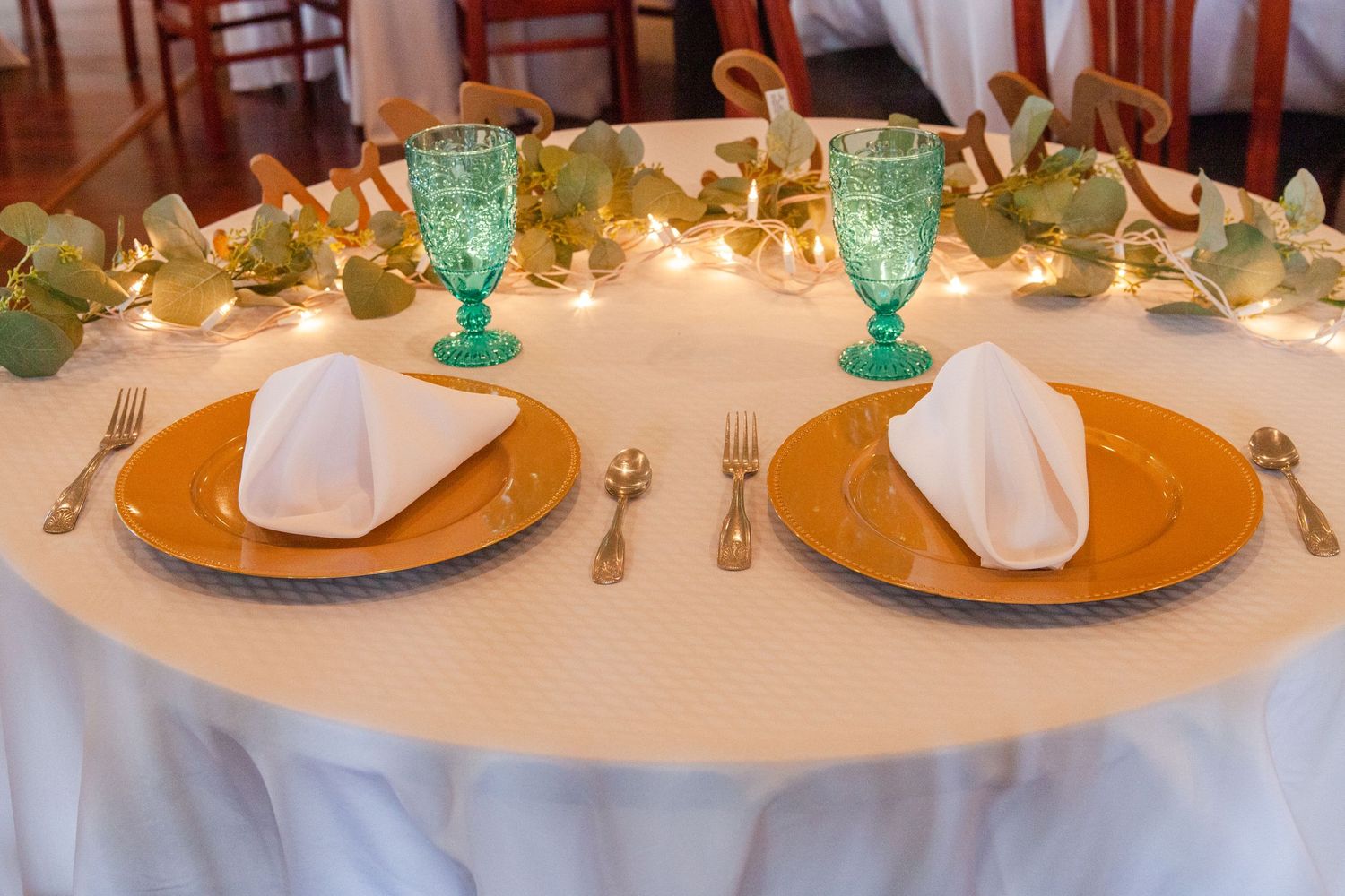 Formal table settings with gold chargers, white napkins and turquoise glassware for wedding reception.