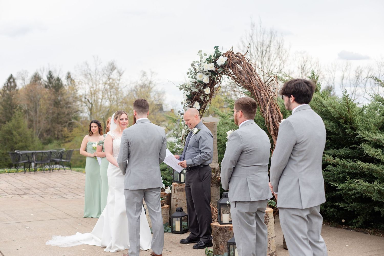 Wedding ceremony participants standing under a decorated arch on a stone patio.