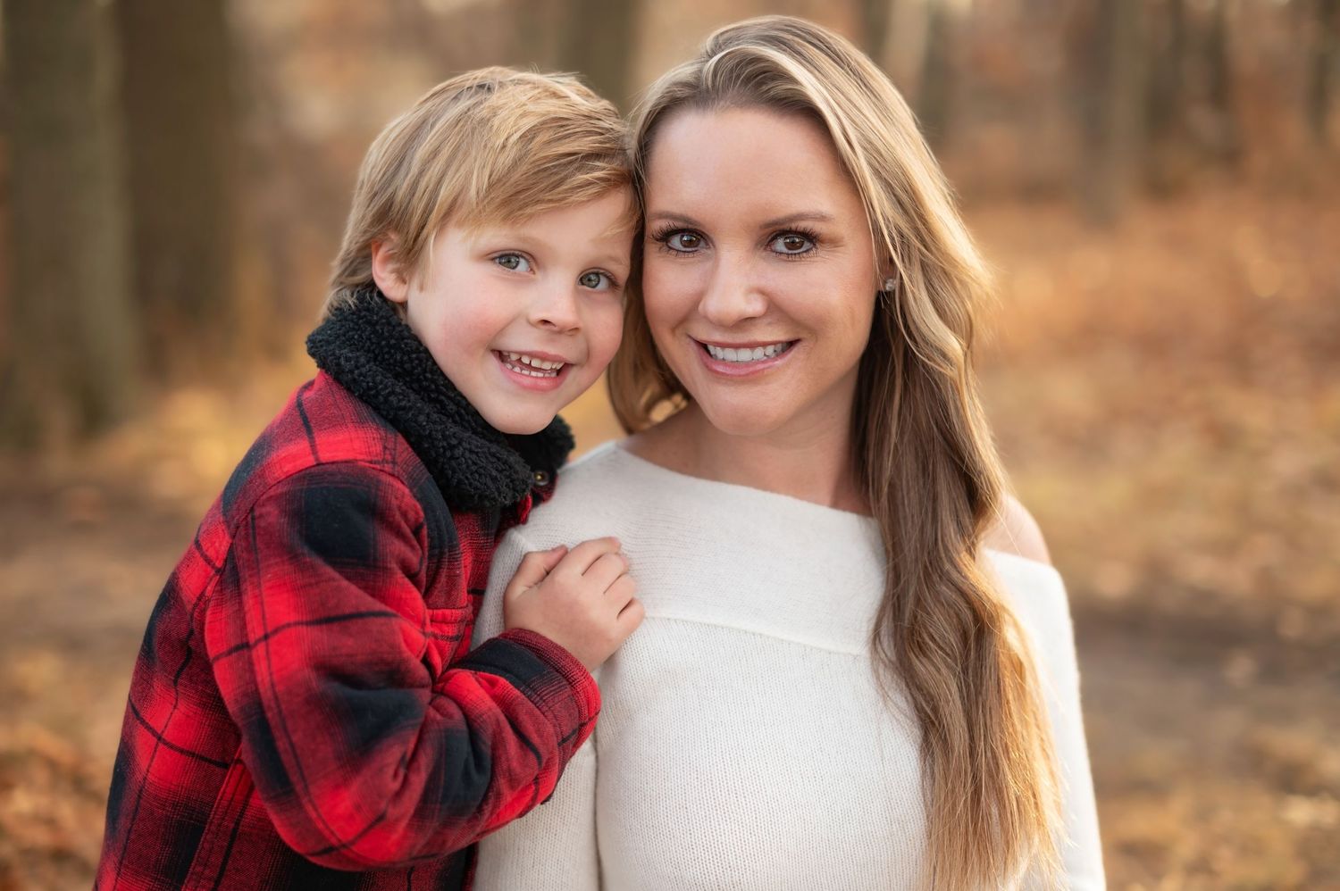 Outdoor autumn portrait showing a close embrace between two people wearing red buffalo plaid and white sweater.