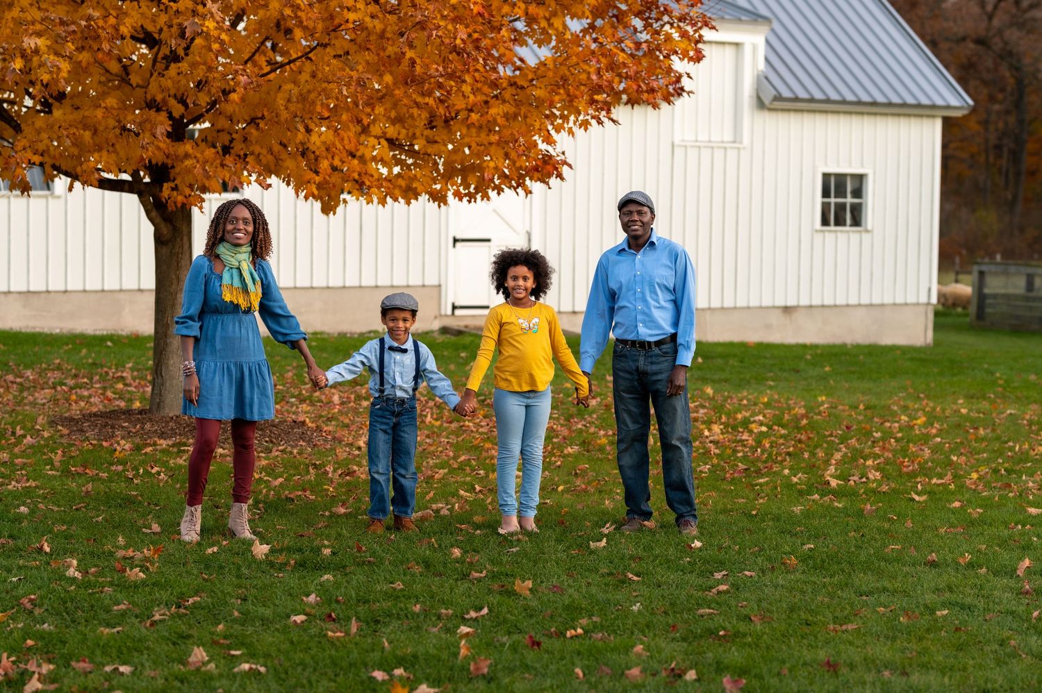 Beautiful fall family portrait in front of a white barn with colorful maple trees.