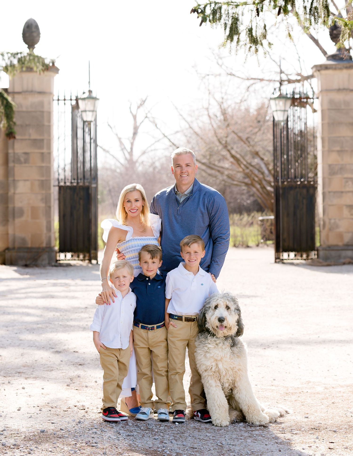 A family with two children and their fluffy white dog pose together in front of ornate stone gates.