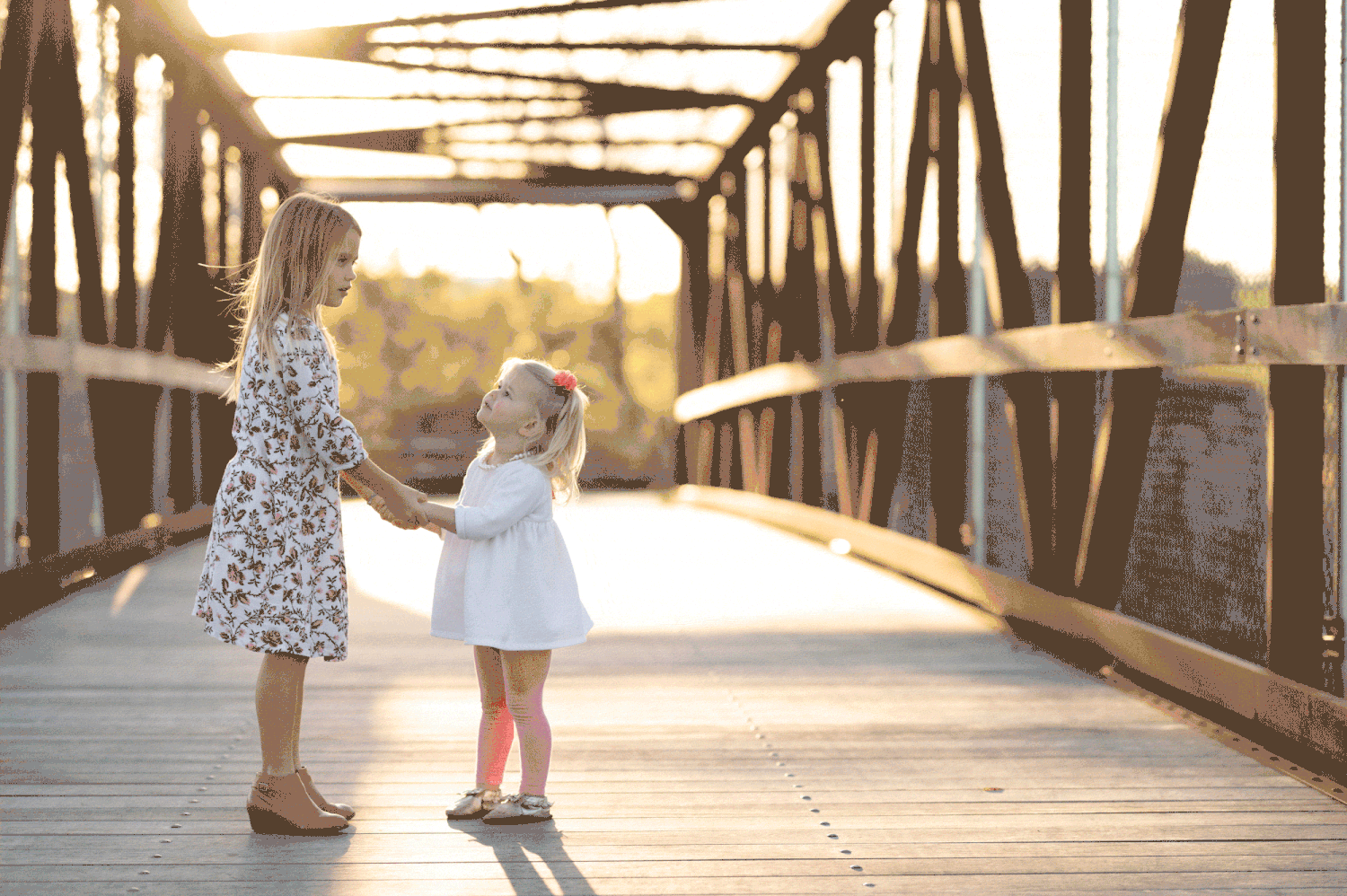 Kids holding hands, playing in a circle on rustic wooden bridge during autumn sunset.