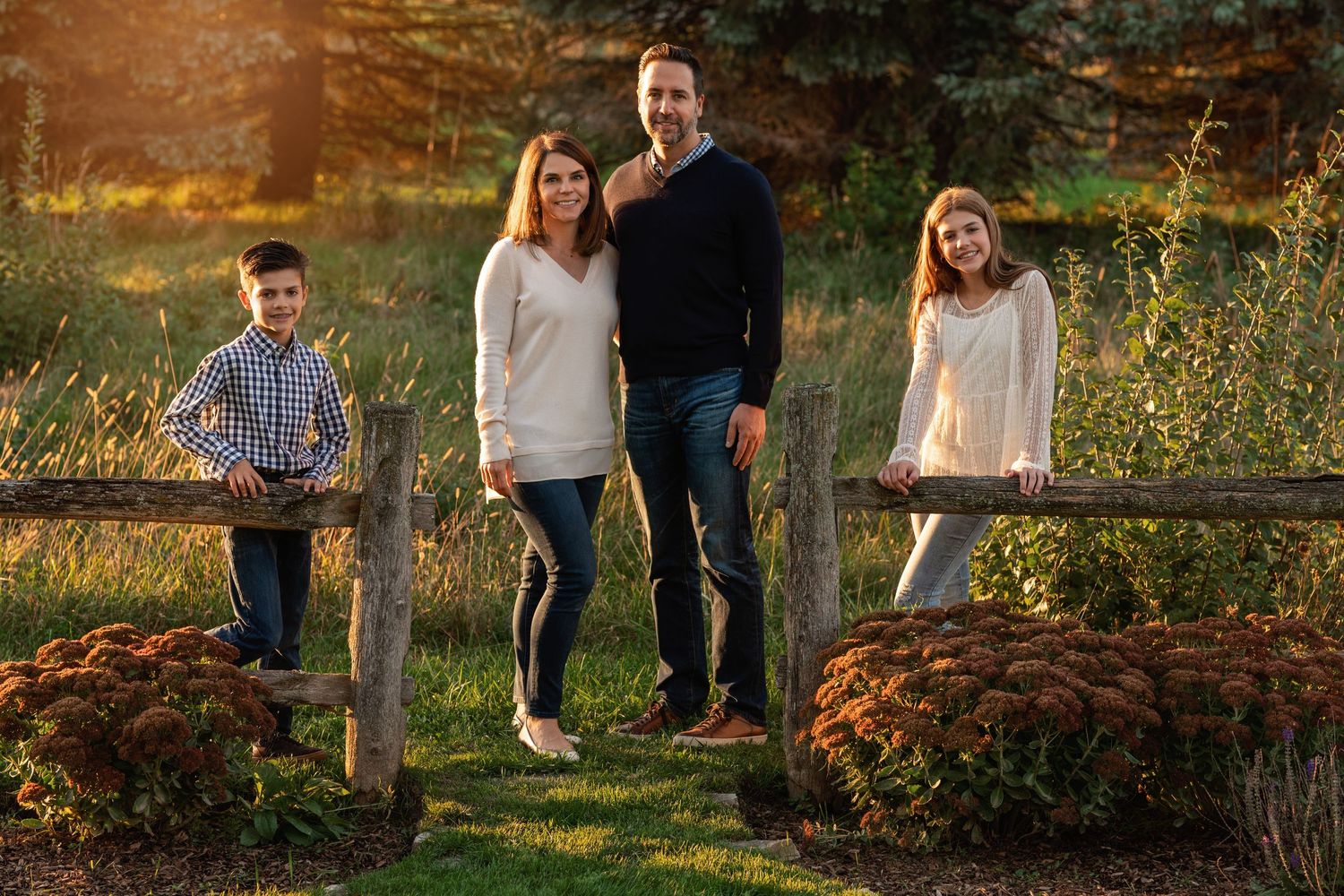 Family posing by rustic wooden fence in autumn garden setting at sunset.