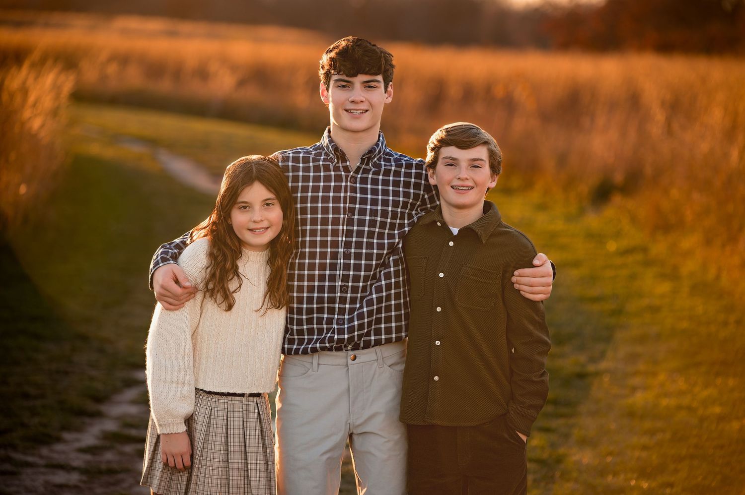 Three siblings pose together at sunset in a field with golden light behind them.