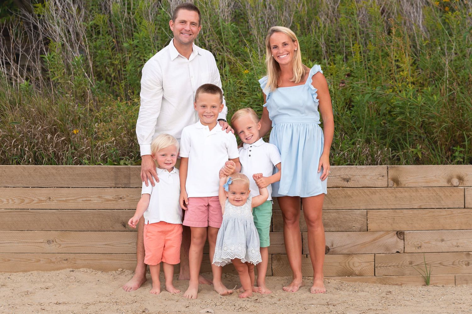 Family standing on wooden steps at beach during summer photo session.