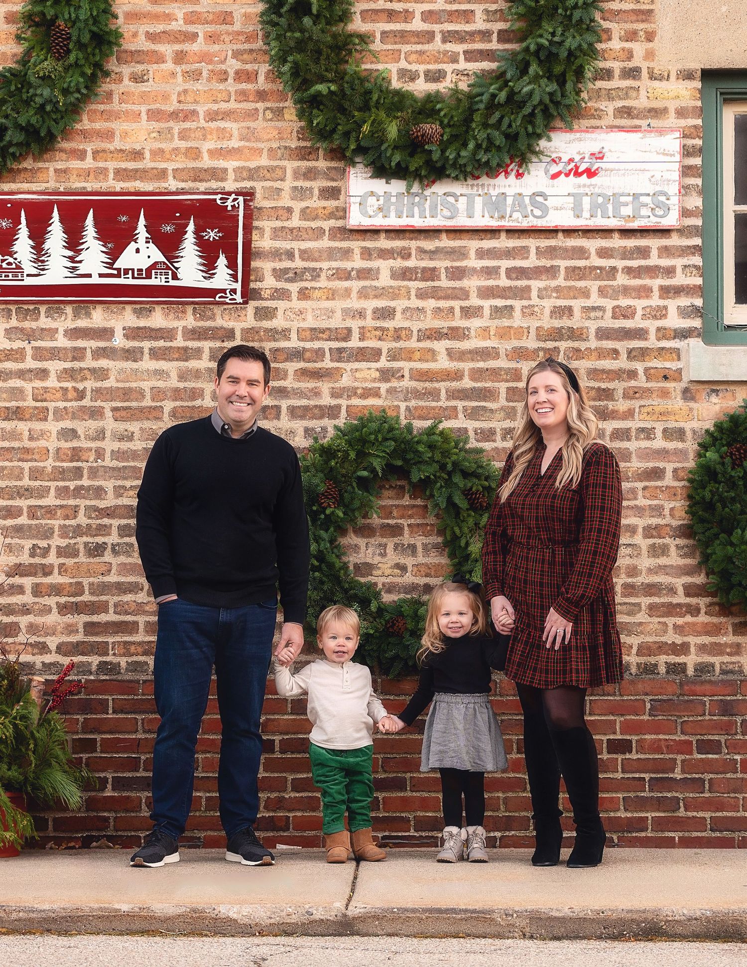 A family poses against a brick wall decorated with Christmas wreaths and holiday decorations.