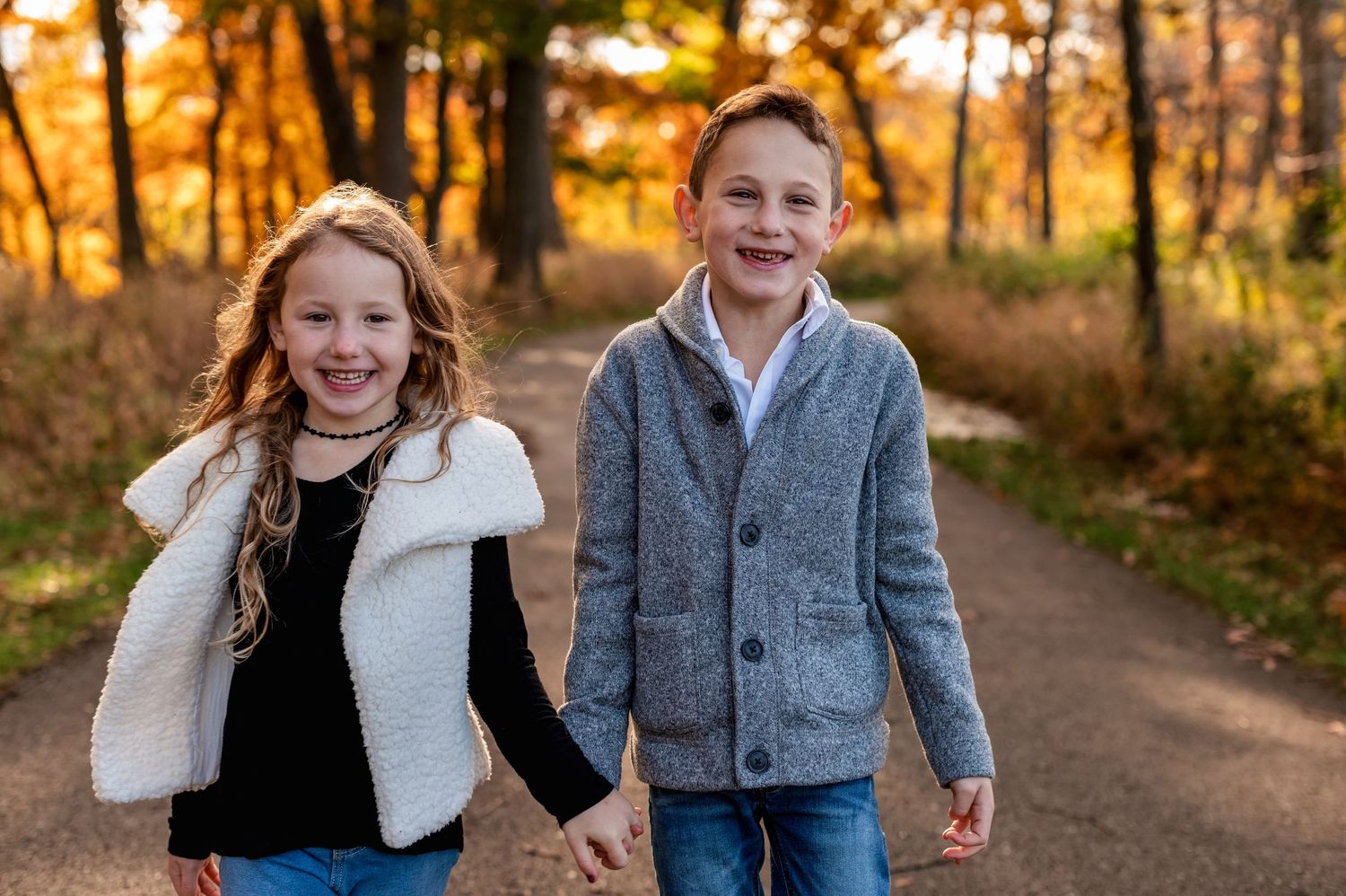 Two children laughing together on an autumn path surrounded by golden foliage.