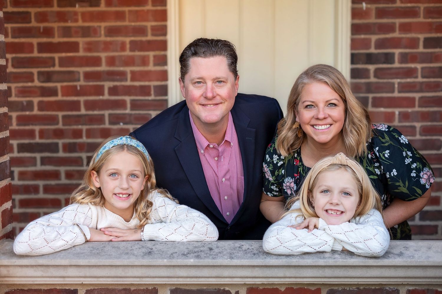 A family leans on wooden railing for portrait with brick building backdrop.