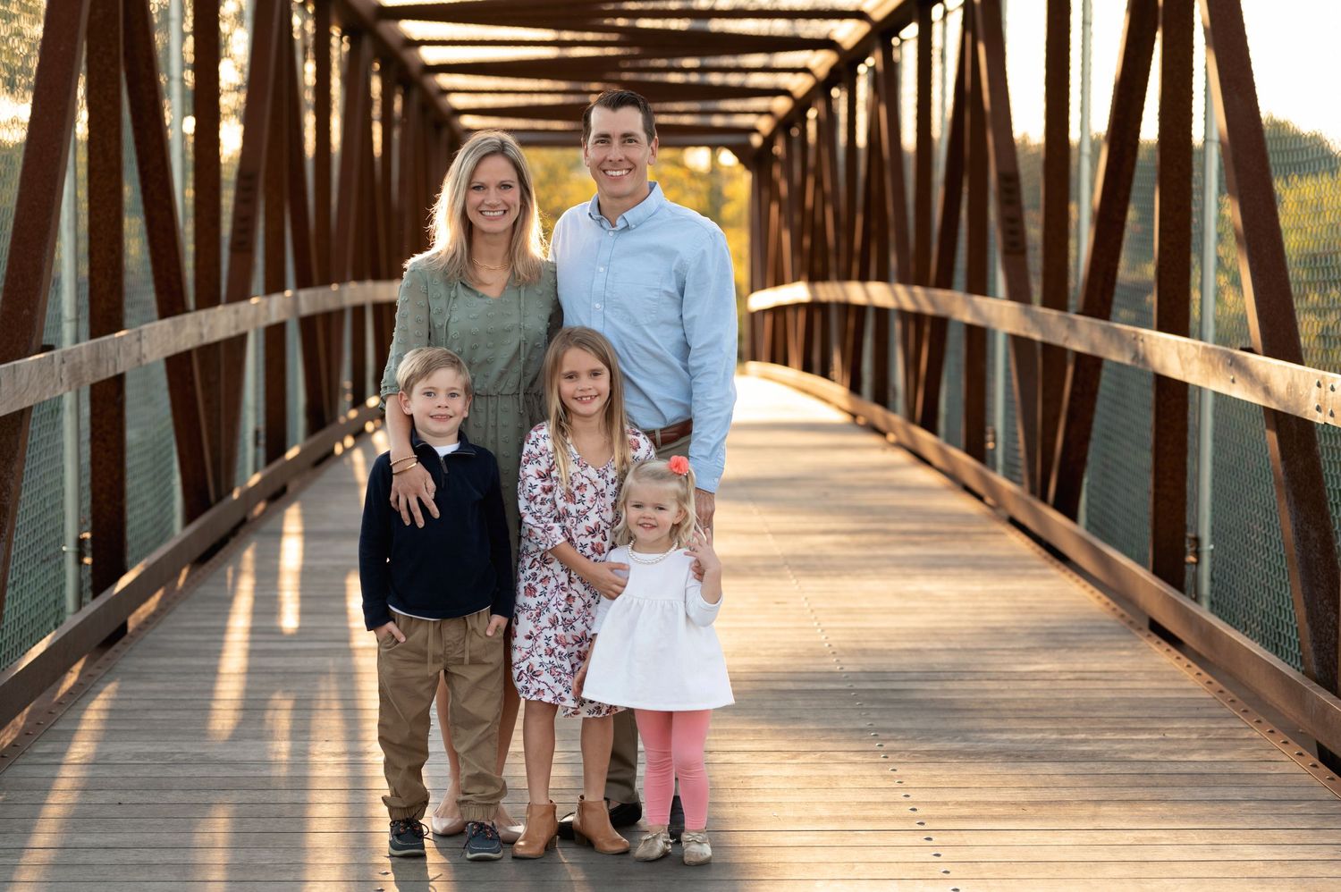 Family portrait on rustic wooden bridge during autumn sunset.