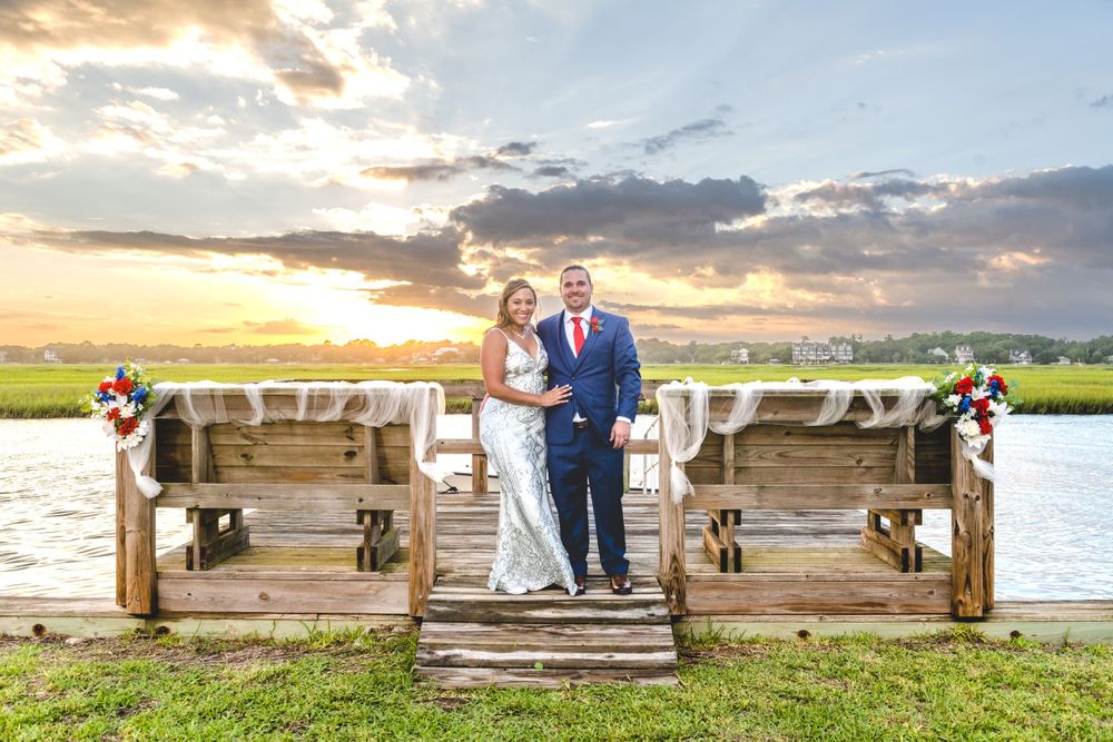 Sunset wedding portrait on wooden dock overlooking coastal marshland with decorated railings.